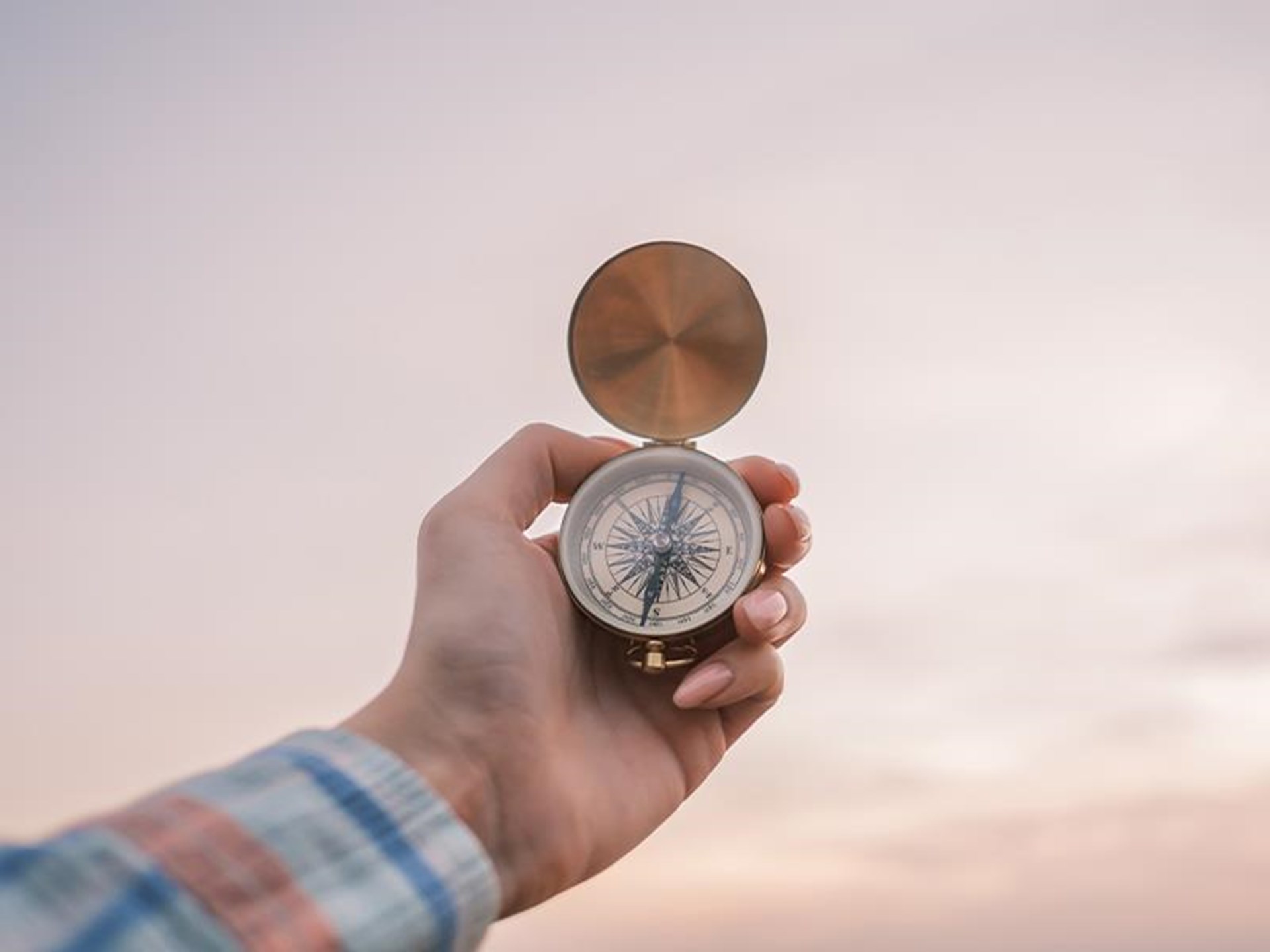 Hand hält einen geöffneten Kompass vor einem hellen Himmel
